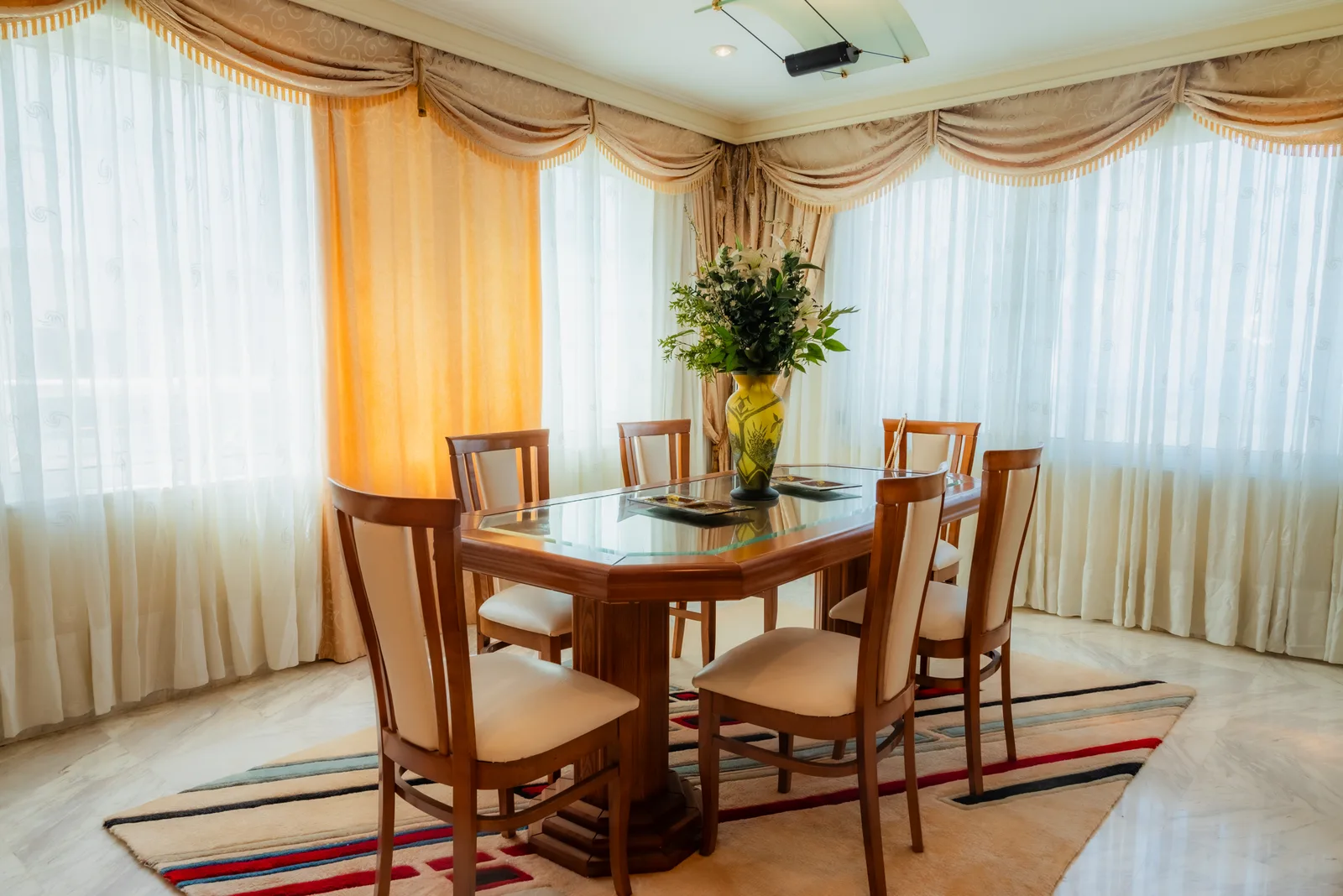 Dining room with a glass table, wooden chairs and yellow curtains