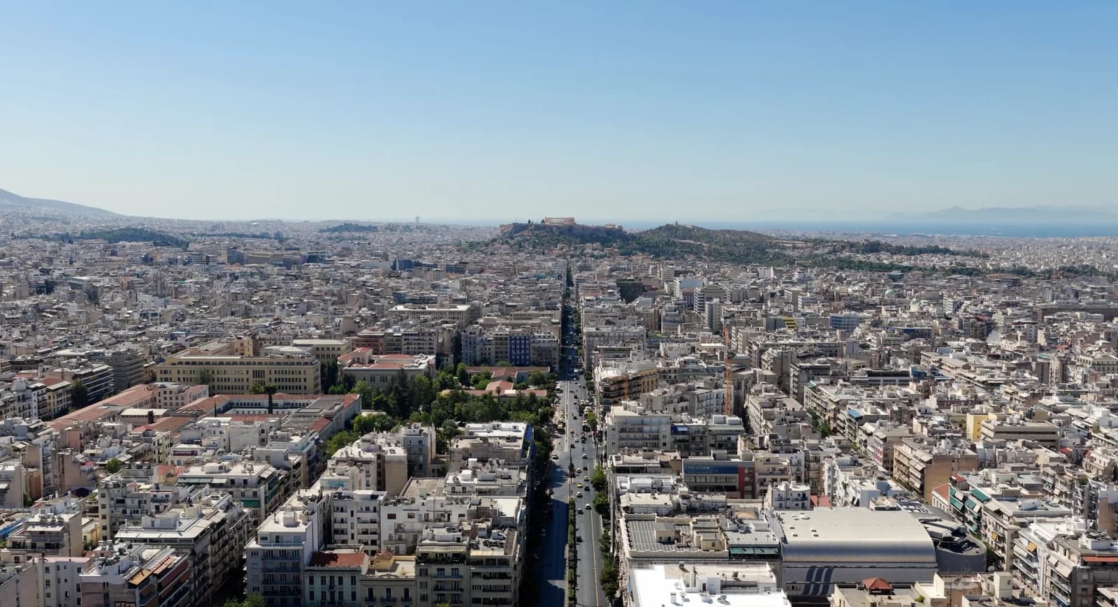 Aerial view over central Athens with a long avenue running toward the Acropolis and the sea beyond it